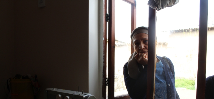 A psychologist with Living with Dignity in Tajikistan looking into an open window into a room with a sewing machine on a table.