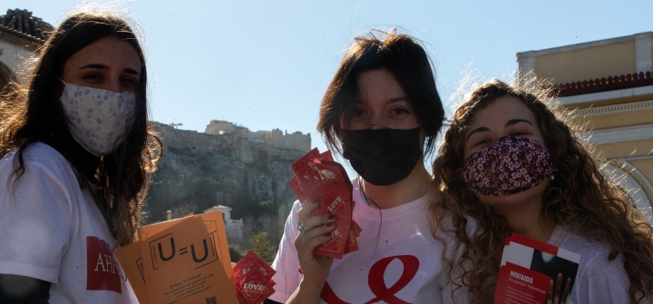 Three female volunteers, wearing cloth face masks, pose with leaflets about sexual health in Athens, Greece, on World AIDS Day, Dec. 1, 2021.