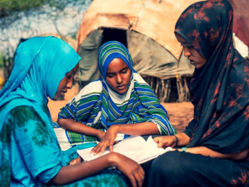 Three girls wearing colorful head scarves sit reading together.