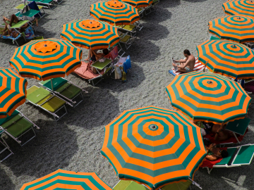 Orange and greenish-blue striped beach umbrellas lined up on an Italian beach with a few people sitting underneath.