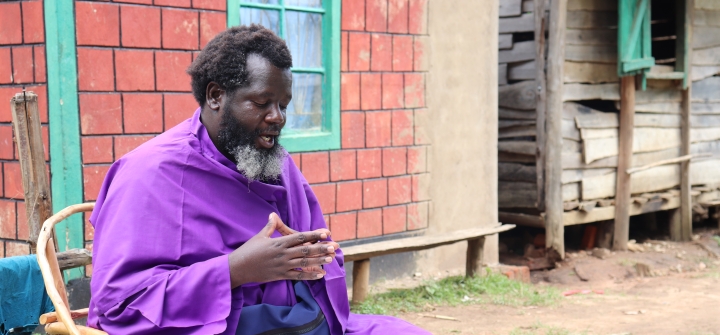  Eliud Wekesa, hands clasped, with a graying beard and wearing a bright purple robe, speaks to visitors outside his home and church compound in Tongaren, Bungoma County, Kenya, on February 29, 2024.