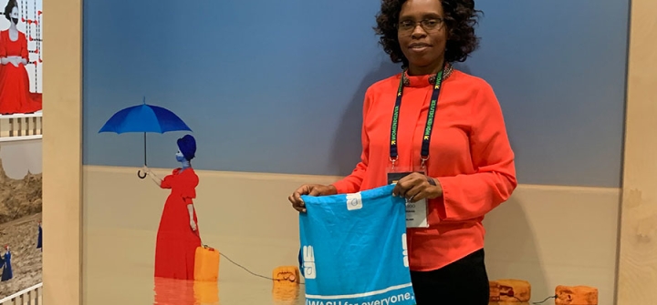 In front of WaterAid's Women Deliver 2019 exhibit booth, WaterAid Malawi Country Director Mercy Masoo holds up a bag with one of their key messages: WASH for everyone.