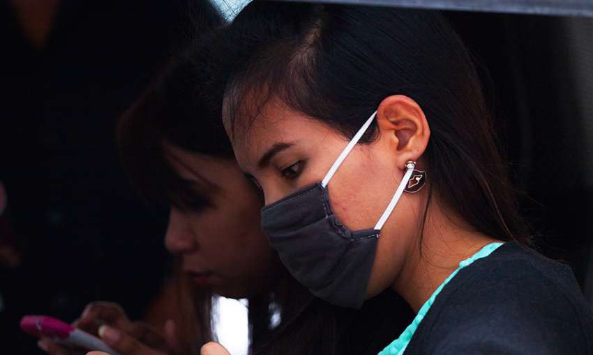 Young Thai girl with mobile and surgical mask. 