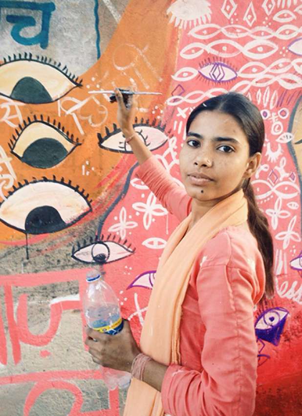 A woman painting a mural with eyes staring back at harassers in New Delhi. 