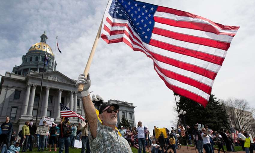 A man waves a US flag in front of the Colorado State Capitol building during a demonstration to protest coronavirus stay-at-home orders.  Denver, April 19, 2020. Image: Jason Connolly/AFP/Getty 