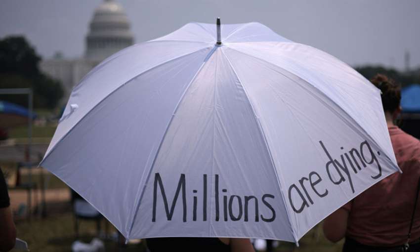 Attendees seek shelter from the sun beneath an umbrella during a COVID-19 prayer vigil. Washington, DC, July 20, 2021. Image: Win McNamee/Getty