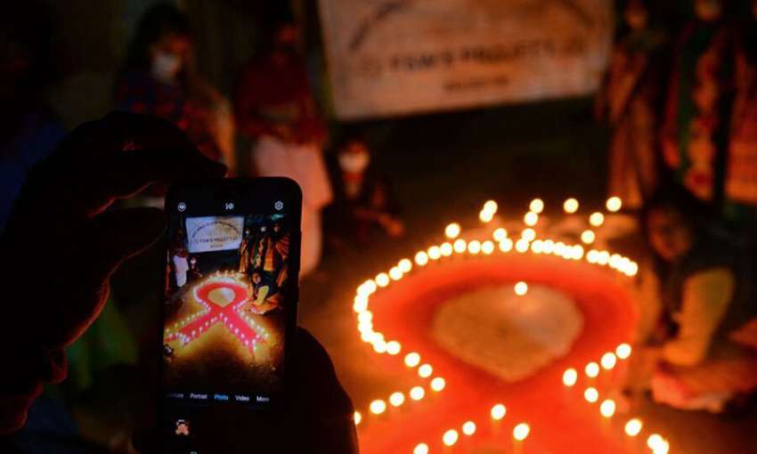 A volunteer takes pictures with her mobile phone of others lighting candles in the shape of a red ribbon during an awareness event on the eve of World AIDS Day in Siliguri, West Bengal, India, on November 30, 2021. 