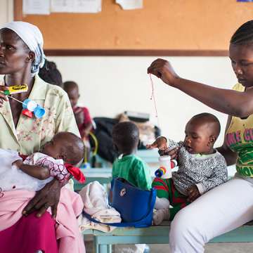 Caretakers in Kenya playing with children in a health facility waiting room (using toys made from locally available materials). 