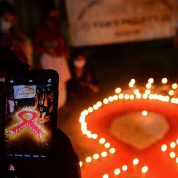 A volunteer takes pictures with her mobile phone of others lighting candles in the shape of a red ribbon during an awareness event on the eve of World AIDS Day in Siliguri, West Bengal, India, on November 30, 2021. 