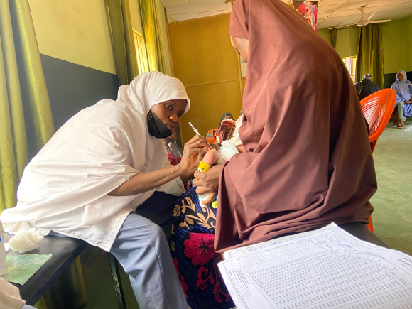 A health worker vaccinates a child held by a mother wearing a rust-colored headscarf in the Farfaru clinic in nothern Nigeria.