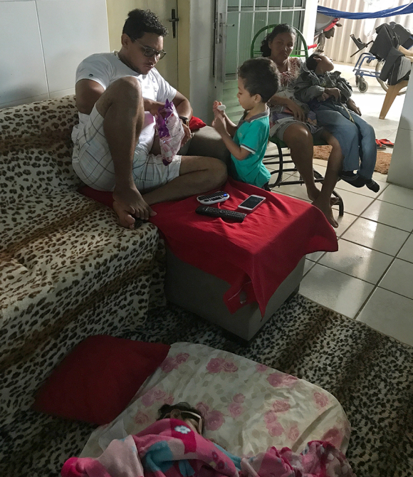 Jorge watches cartoons and eats marshmallows with his stepfather, Luiz Carlos Ribeiro Valadares Junior, while Valentina naps on a mattress near him