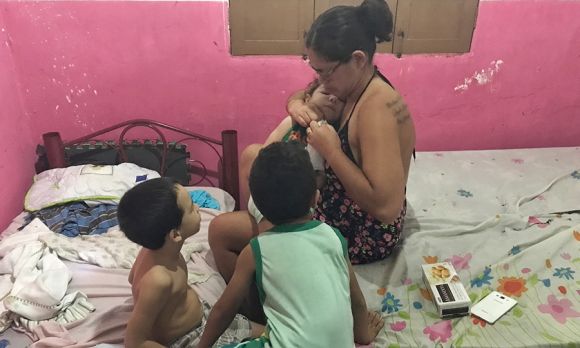 Mylene Helena dos Santos Ferreira, 23, opens a package of chocolate biscuits for her eager sons while balancing Davi in her lap.